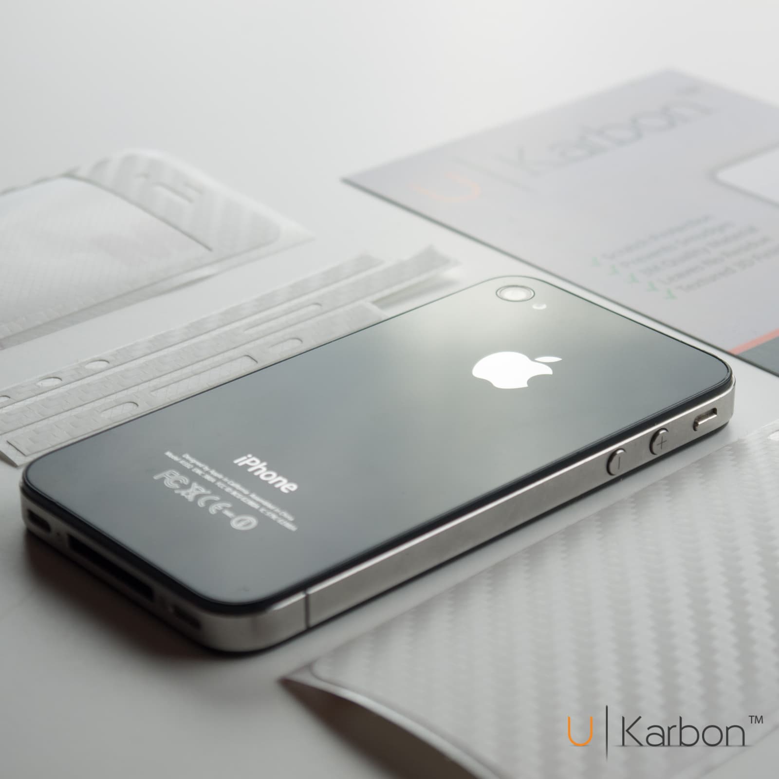 An iPhone 4 with a UKarbon skin alongside branded packaging and application tools